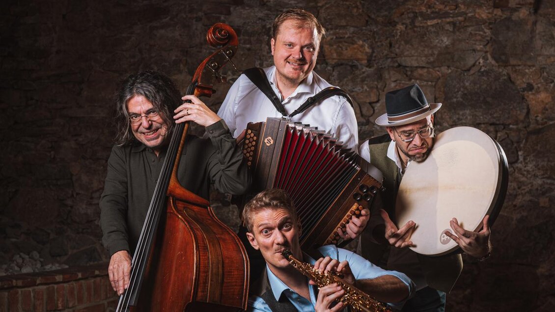 Eine Gruppe von vier Musikern posiert in einem alten Raum. Sie spielen verschiedene Instrumente wie Kontrabass, Akkordeon und Flöte. | © reithofer_media