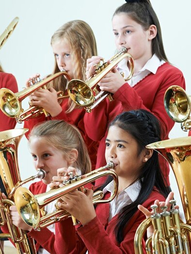 A group of children is playing trumpet and trombone together. They are wearing red sweaters and focusing on their music.