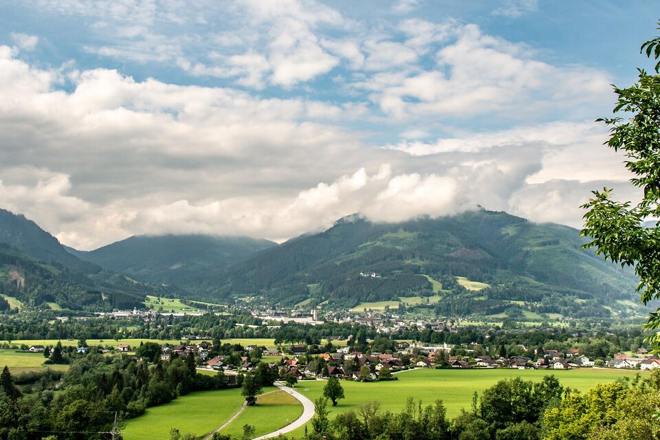 Eine malerische Landschaft mit grünen Wiesen und majestätischen Bergen im Hintergrund. Ein einzelner Baum steht vor einem kleinen Dorf, das von der Natur umgeben ist. | © TV Gesäuse
