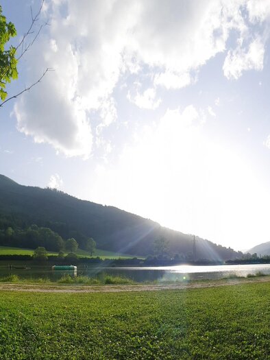 A peaceful landscape with a lake and gentle hills in the background. The sky is clear and the sun is shining bright. | © Gemeinde Wald am Schoberpaß