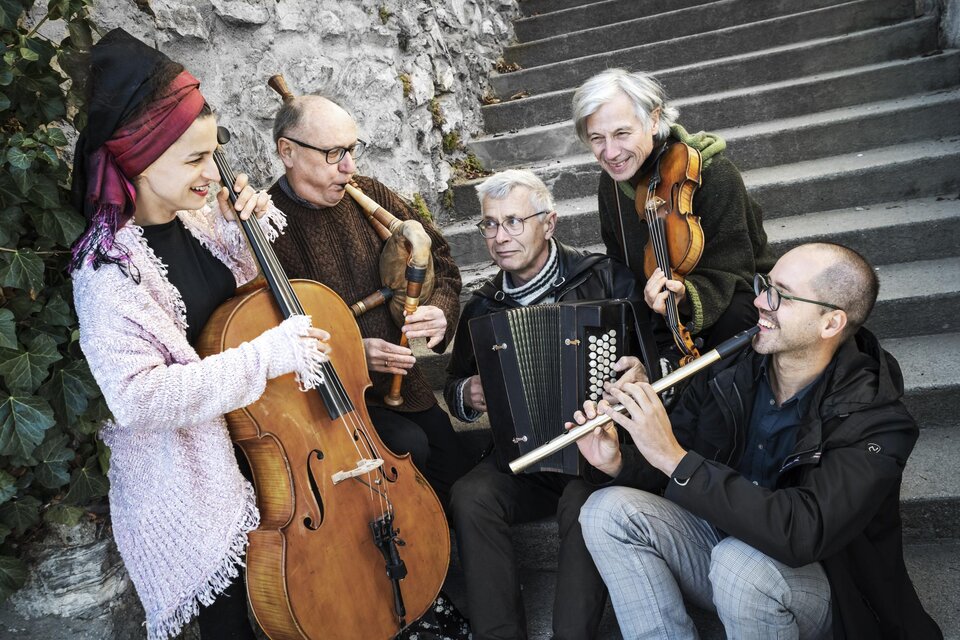 Eine Gruppe von fünf Musikern spielt verschiedene Instrumente auf einer Treppe. Sie lächeln und wirken fröhlich in einer gemütlichen Atmosphäre. | © Ulrike_Rauch