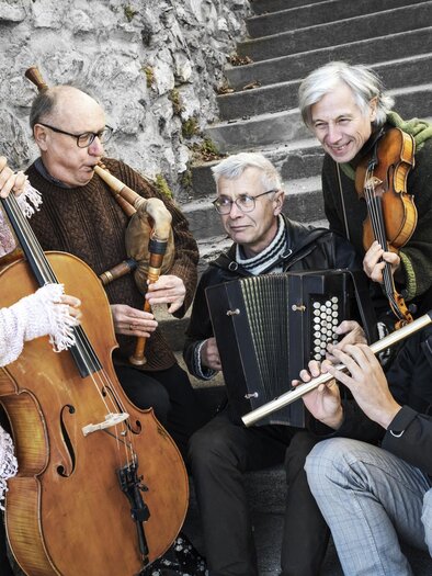 Eine Gruppe von fünf Musikern spielt verschiedene Instrumente auf einer Treppe. Sie lächeln und wirken fröhlich in einer gemütlichen Atmosphäre. | © Ulrike_Rauch