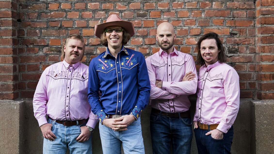Eine Männergruppe steht vor einer Backsteinwand. Sie tragen westernähnliche Hemden und Cowboyhüte. | © Prenninger