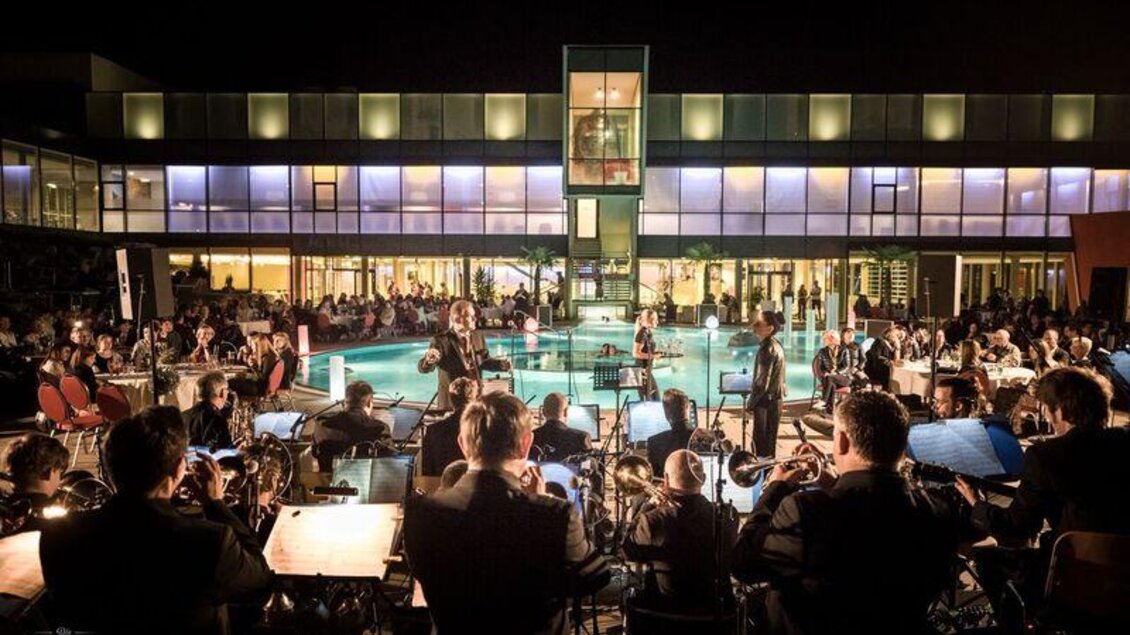 Die Big Band Köflach spielt in der Therme NOVA, im Hintergrund ein Thermalbecken und das Thermengebäude. | © Die Abbilderei