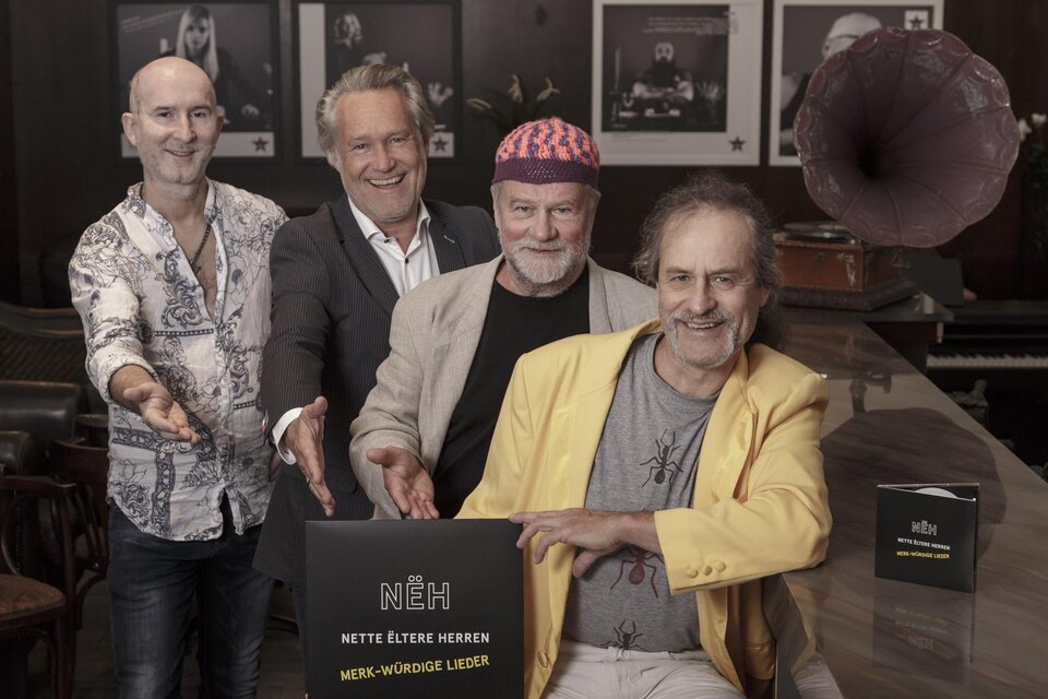 Vier Männer stehen an einem Tisch und lächeln in die Kamera. Sie präsentieren ein Album mit dem Titel "NÉH – Nettes Ältere Herren". | © Weinberger