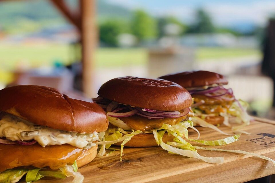 Drei leckere Burger auf einem Holzbrett. Die Brötchen sind frisch und mit Salat und Zwiebeln belegt. | © Steirerhütte