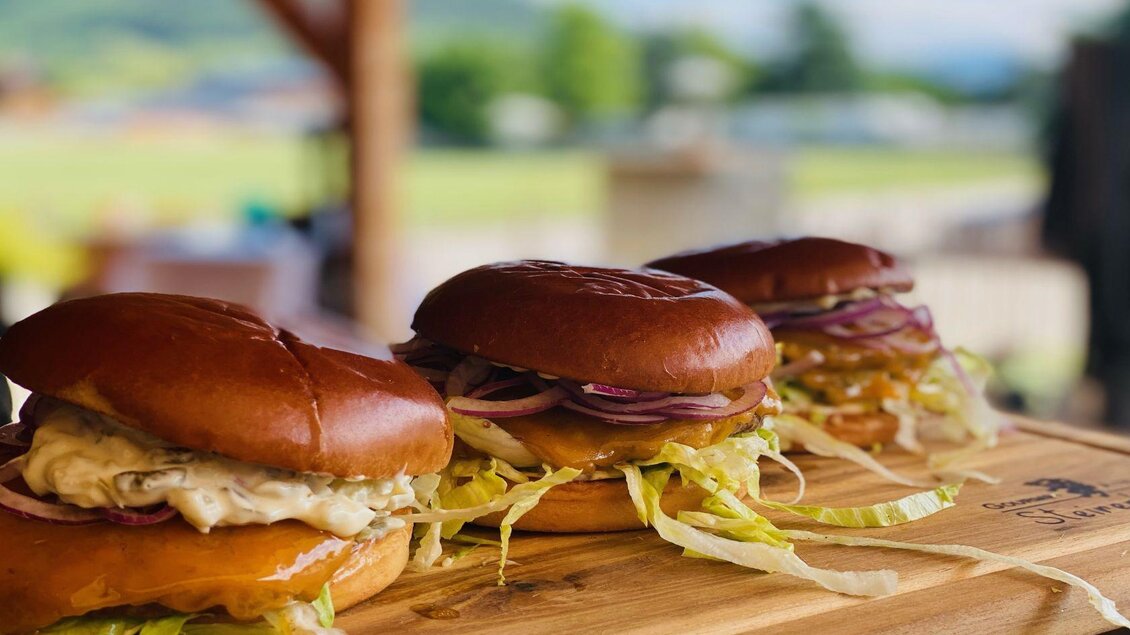 Drei leckere Burger auf einem Holzbrett. Die Brötchen sind frisch und mit Salat und Zwiebeln belegt. | © Steirerhütte