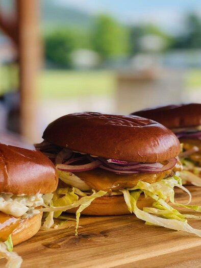 Three delicious burgers on a wooden board. The buns are fresh and topped with lettuce and onions. | © Steirerhütte