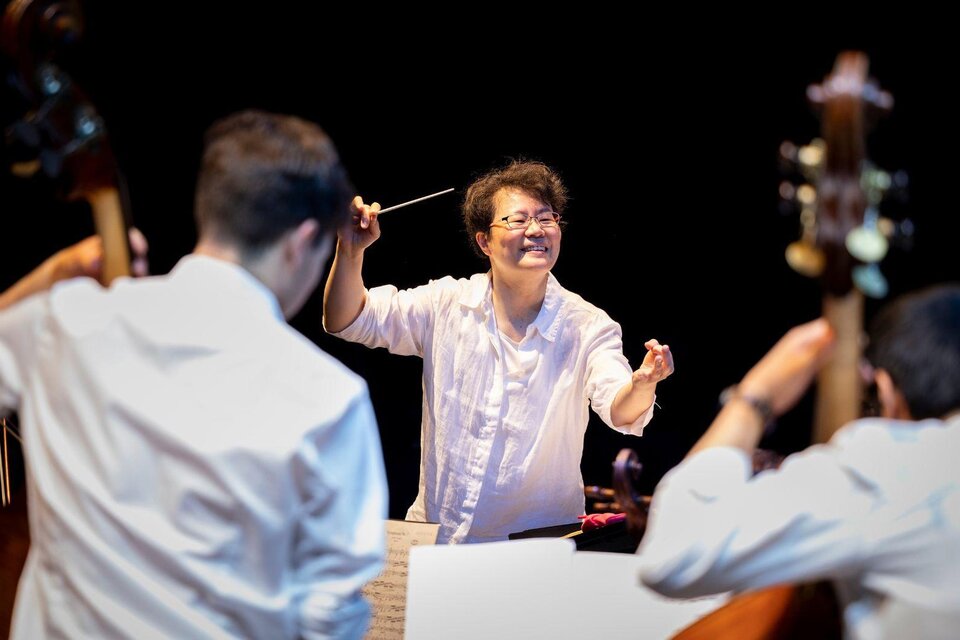 Ein Dirigent leitet ein Orchester mit Begeisterung. Im Hintergrund sind Musiker mit ihren Instrumenten zu sehen. | ©  Nikola Milatovic
