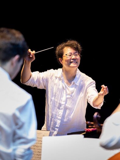 A conductor passionately leads an orchestra. In the background, musicians with their instruments can be seen. | ©  Nikola Milatovic