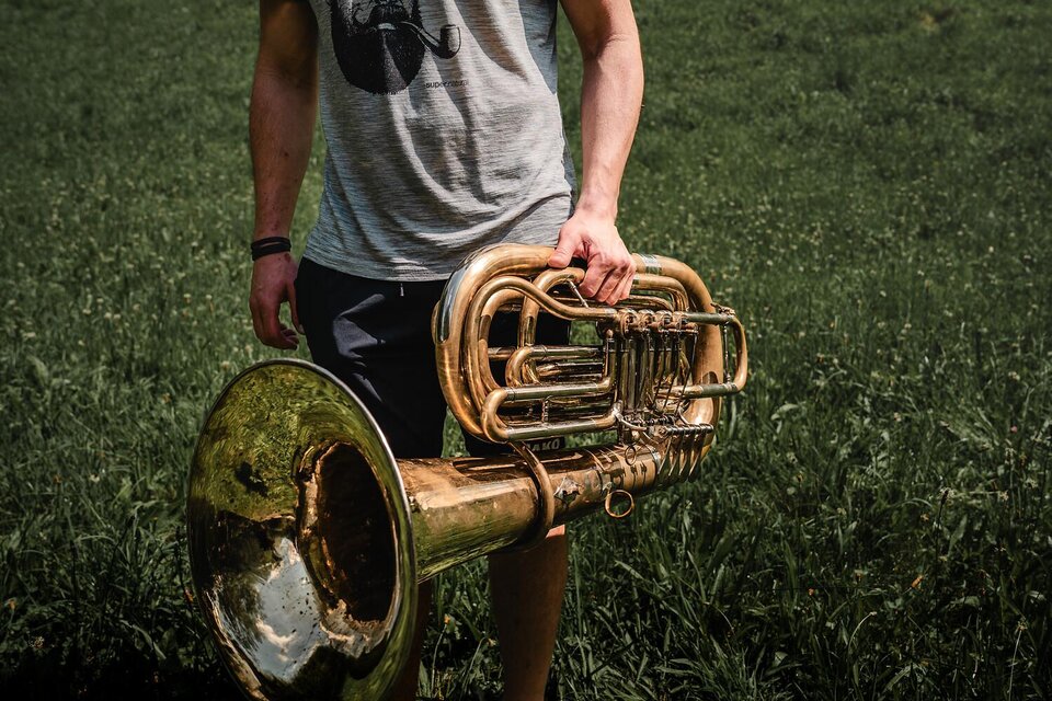 Eine Person hält eine glänzende Tuba in einem grünen Feld. Im Hintergrund sind hohe Gräser zu sehen. | © Archiv TV Gesäuse