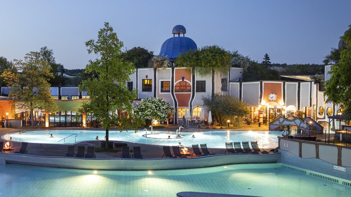 Ein schöner Außenbereich mit einem Pool und einer markanten Architektur. Der Himmel ist klar, und die Umgebung ist von Bäumen umgeben. | © Rogner Bad Blumau © Hundertwasser Architekturprojekt