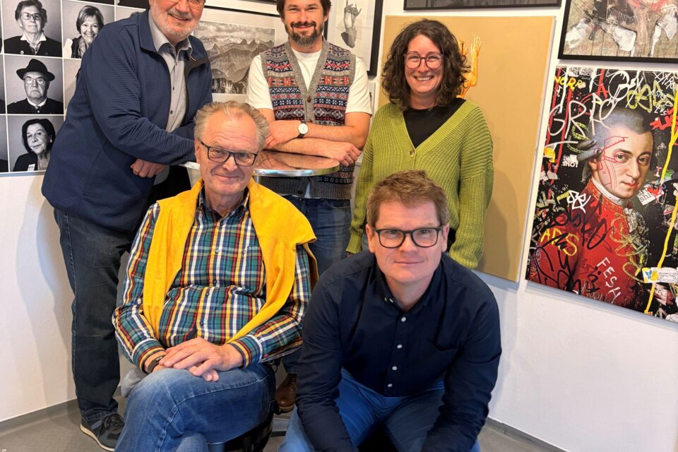 Eine Gruppe von fünf Personen posiert in einem Raum mit vielen Kunstwerken an der Wand. Die Atmosphäre wirkt freundlich und kreativ. | © KI Kürbis Wies