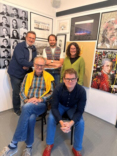 Eine Gruppe von fünf Personen posiert in einem Raum mit vielen Kunstwerken an der Wand. Die Atmosphäre wirkt freundlich und kreativ. | © KI Kürbis Wies