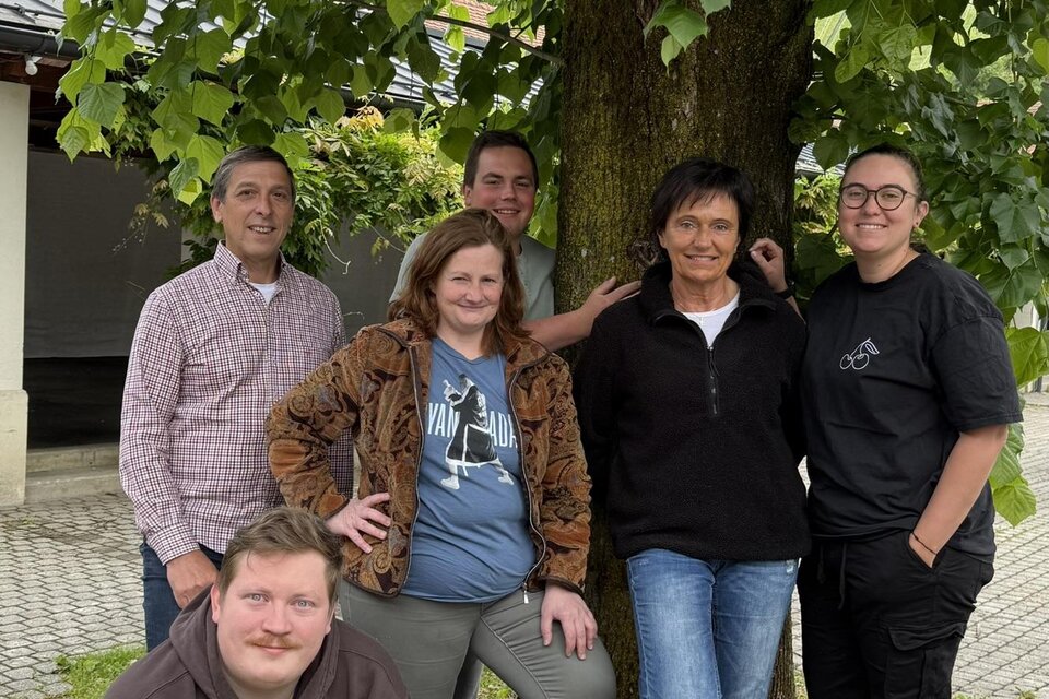 Eine Gruppe von sechs Personen steht lächelnd unter einem Baum. Sie posieren gemeinsam im Freien und wirken freundlich und entspannt. | © Annelies Strauß-Held