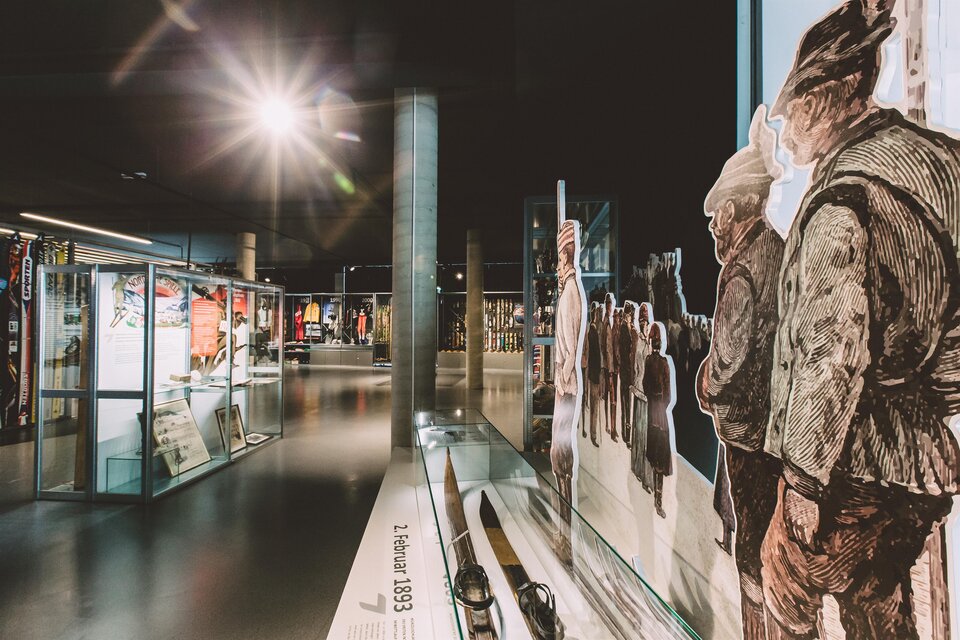 Ein modernes Museum mit Ausstellungsstücken in Vitrinen und Wandmalereien von Menschen. Die Beleuchtung schafft eine einladende Atmosphäre. | © nicoleseiser.at