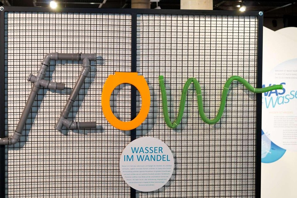 Eine kreative Installation mit dem Wort "FLOW", das aus Rohren und Schläuchen besteht. Darunter steht der Text "WASSER IM WANDEL". | © WinterSportMuseum