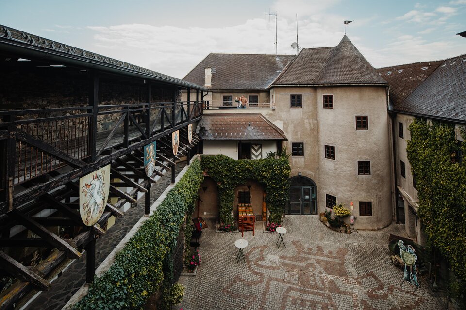 Ein historischer Innenhof mit alten Gebäuden und grünem Efeu. Der Platz ist mit Steinen gestaltet und es gibt einige Sitzgelegenheiten. | © nicoleseiser.at
