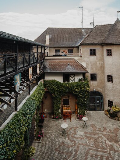 Ein historischer Innenhof mit alten Gebäuden und grünem Efeu. Der Platz ist mit Steinen gestaltet und es gibt einige Sitzgelegenheiten. | © nicoleseiser.at