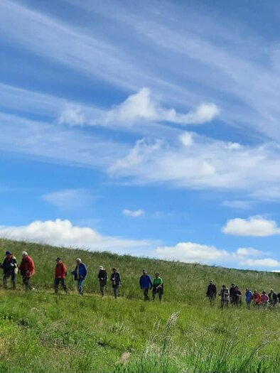 Eine Gruppe von Wanderern geht einen Hügel hinauf. Der Himmel ist blau mit einigen Wolken und die Landschaft ist grün und weitläufig. | © Anna Maria Ladler