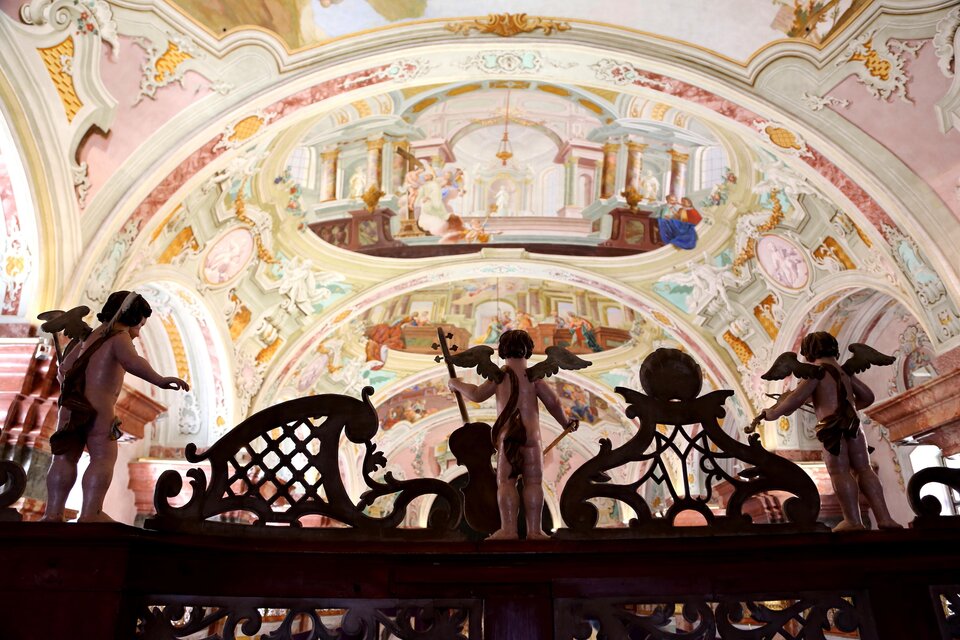 Eine herrliche Decke mit farbenfrohen Fresken und vergoldeten Details. Im Vordergrund sind kunstvolle Holzfiguren von Engeln zu sehen. | © Stift Rein