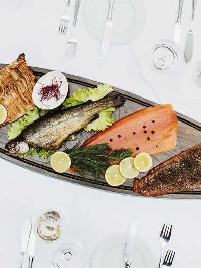 Ein dekorativer Fisch-Teller mit verschiedenen zubereiteten Fischen und frischen Zutaten. Der Tisch ist elegant gedeckt mit Besteck und Gläsern. | © Begsteiger