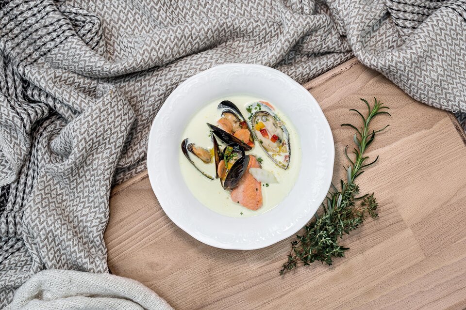 Ein schönes Gericht mit Muscheln und Lachs in einer cremigen Sauce. Das Essen ist auf einem weißen Teller angerichtet und von einem gemütlichen Tuch umgeben. | © Fischrestaurant Kulmer
