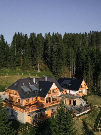 Egy kényelmes faház a magas fenyőfák között. A környezet zöld és hívogató, tökéletes egy nyugodt visszavonuláshoz. | © Weizerhütte