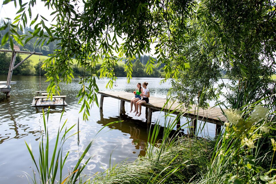 Ein wunderschöner Steg am See mit zwei Personen, die sitzen und die Aussicht genießen. Umgeben von üppigem Grün und ruhigem Wasser, strahlt die Szenerie Entspannung und Naturverbundenheit aus. | © Tv Murau
