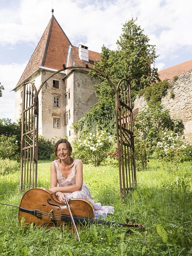Eine Frau sitzt im Gras vor einer alten Mauer und einem Torbogen. Im Hintergrund ist ein historisches Gebäude zu sehen. | © Werner Kmetitsch