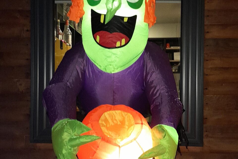 Eine leuchtende Halloween-Dekoration zeigt eine grüne Hexe mit lila Kleid und orangefarbenem Hut. Sie hält einen leuchtenden Kürbis in den Händen. | © Mountain Adventure Golf