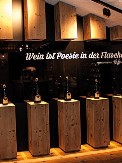 Ein stilvoller Weinkeller mit Holzregalen und edlen Weinflaschen. An der Wand steht der Schriftzug: "Wein ist Poesie in der Flasche." | © Karin Moser|Spross Fest