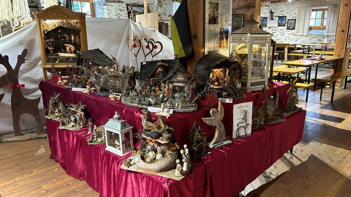 Ein hübscher Stand mit kunstvoll gestalteten Weihnachtskrippen und Figuren. Der Tisch ist mit rotem Tuch bedeckt und steht in einem rustikalen Raum.