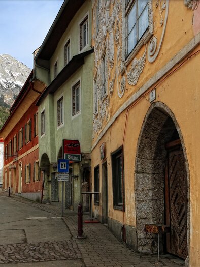 A historic building with decorative facade paintings and windows. In the background, mountains can be seen against a clear sky. | © Pezmann