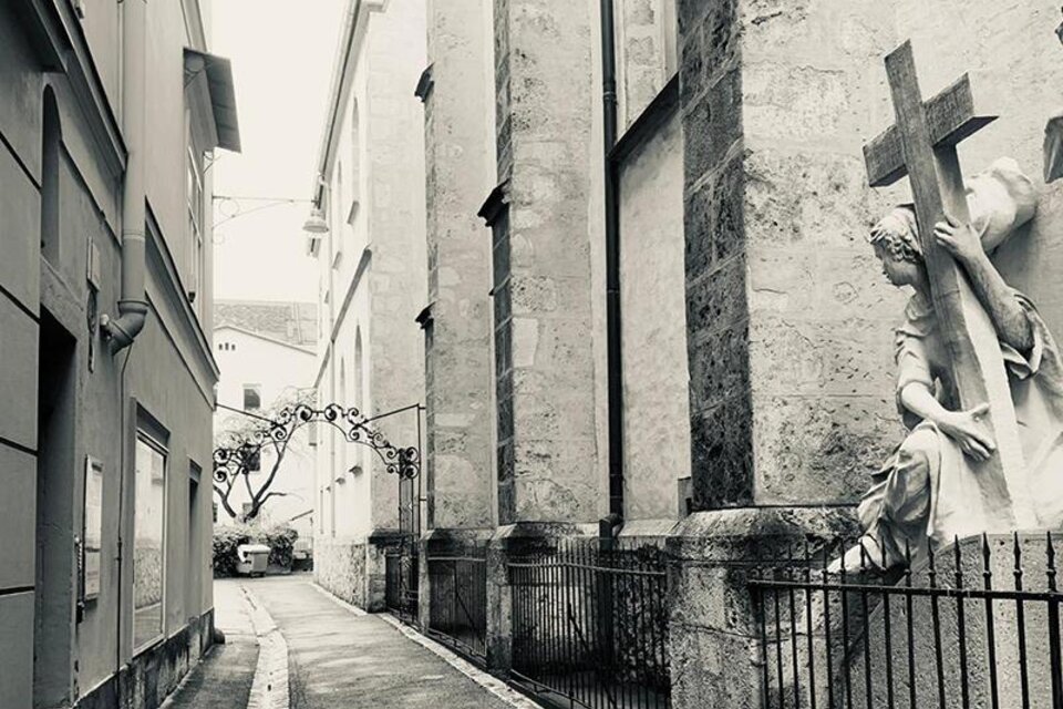 Schwarz-weiß-Foto einer engen Gasse mit Kreuzstatue in der Grazer Altstadt. | © GrazGuides