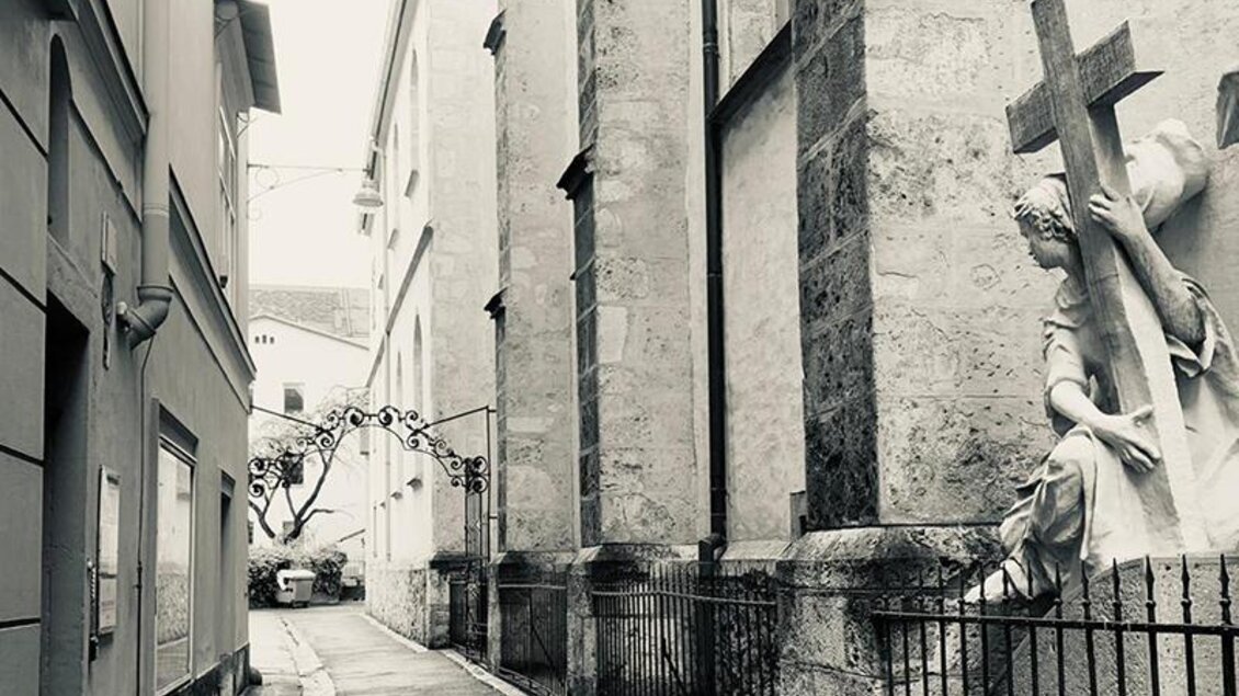 Schwarz-weiß-Foto einer engen Gasse mit Kreuzstatue in der Grazer Altstadt. | © GrazGuides