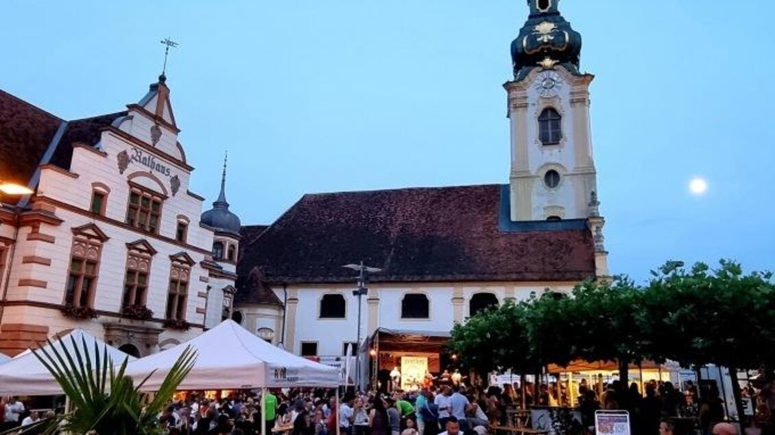 Ein belebter Platz mit vielen Menschen und Festzelten. Im Hintergrund ist eine beeindruckende Kirche zu sehen, unter einem klaren Abendhimmel. | © Oststeiermark Tourismus