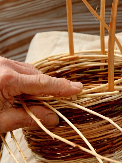 Eine Hand formt einen geflochtenen Korb aus Naturmaterialien. Der Korb hat eine kunstvolle Struktur und zeigt handwerkliches Geschick. | ©  AdobeStock_359694212