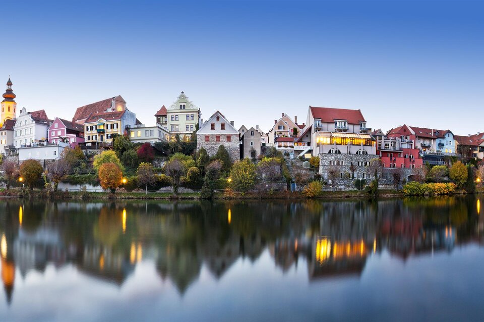 Ein malerisches Dorf am Ufer eines ruhigen Sees, umgeben von sanften Hügeln. Die bunten Häuser spiegeln sich im Wasser und schaffen eine bezaubernde Atmosphäre. | © Rene Vidalli