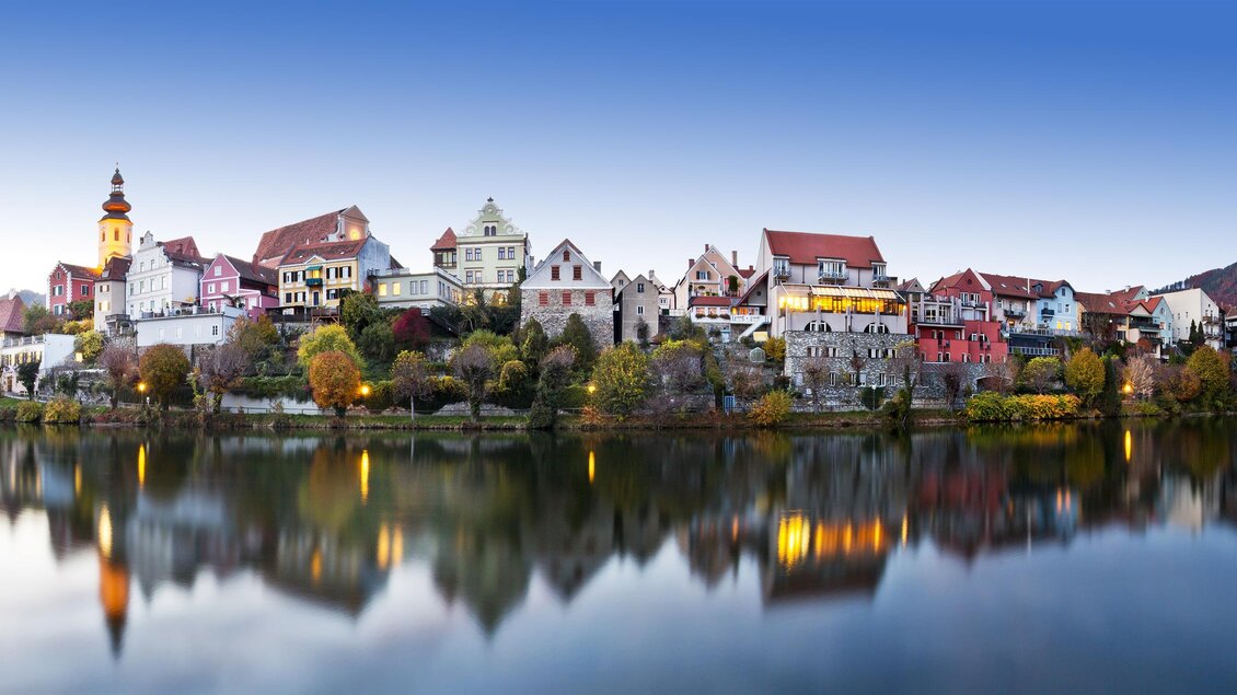 Ein malerisches Dorf am Ufer eines ruhigen Sees, umgeben von sanften Hügeln. Die bunten Häuser spiegeln sich im Wasser und schaffen eine bezaubernde Atmosphäre. | © Rene Vidalli