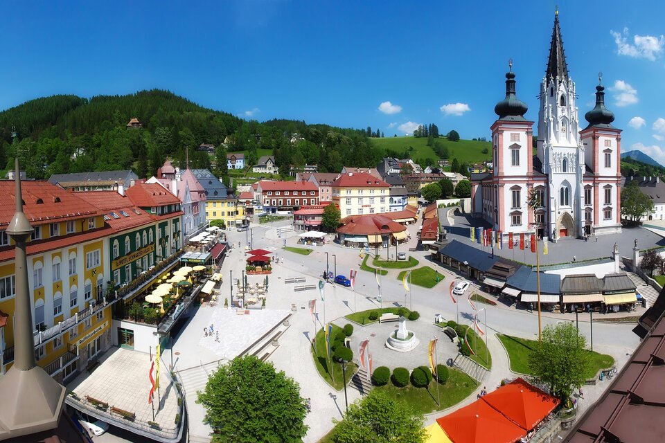 Ein malerischer Marktplatz mit bunten Gebäuden und einer beeindruckenden Kirche im Hintergrund. Die Umgebung ist grün und einladend, ideal für einen Spaziergang. | © Fred Lindmoser