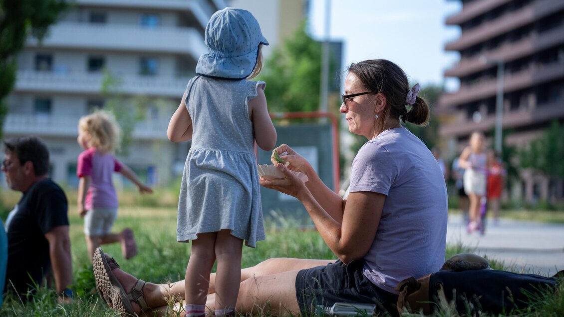 Frau und Kind auf einer Wiese beim Stadtteilfest Reininghaus in Graz vor Wohngebäuden. | © Peter Hutter
