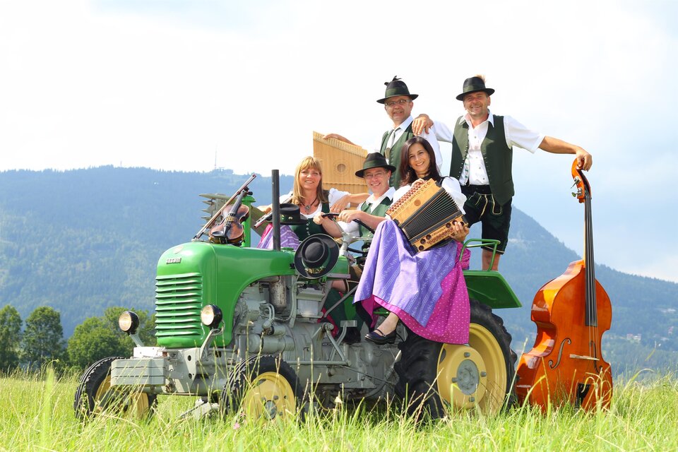 Musikgruppe Knöpferlstreich in Tracht mit Knöpferlharmonika und weiteren Instrumenten auf einem Oldtimer-Traktor beim Stattegger Kultursommer. | © Knöpferlstreich