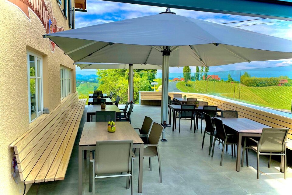 Eine einladende terrasse mit Tischen und Stühlen unter einem großen Sonnenschirm. Im Hintergrund sind grüne Wiesen und ein blauer Himmel zu sehen. | © Eckbergerhof