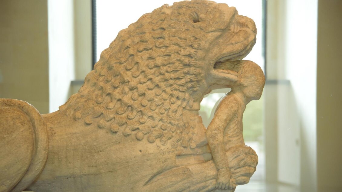Eine eindrucksvolle Skulptur eines Löwen, der eine Person in seinem Maul hält. Die Statue zeigt Details in den Texturen von Körper und Gesicht. | © Heinz Mitteregger