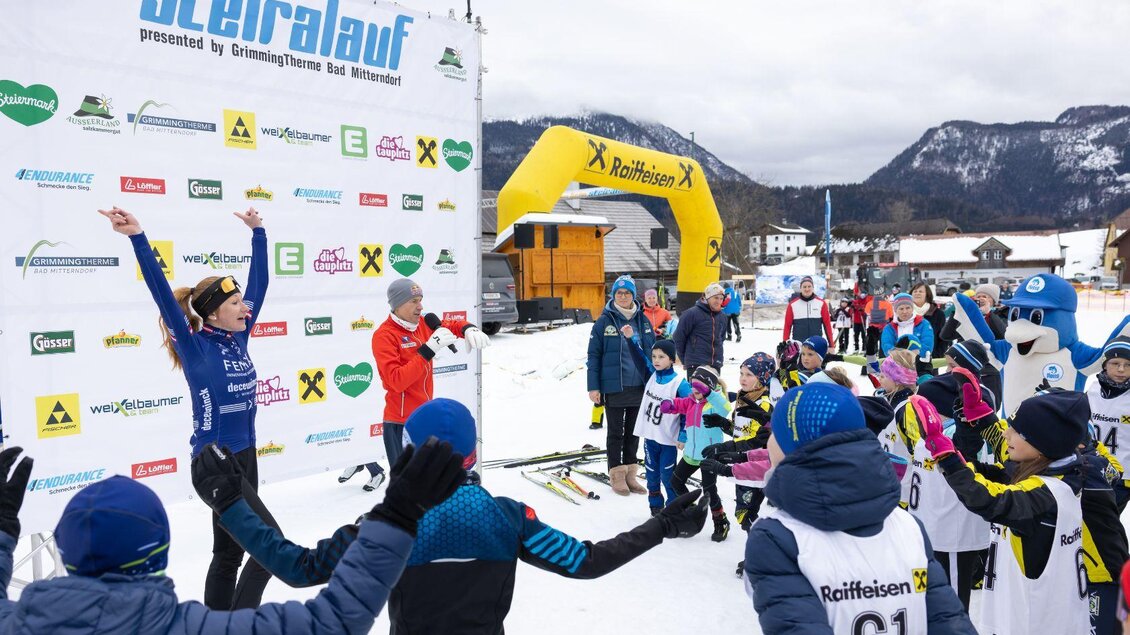 Gemeinsames Aufwärmen mit dem ehemaligen Skispringer Andi Goldberger und Flosse von Aldiana. Vor einer verschneiten Winterlandschaft stehen die Kinder im Halbkreis und bereiten sich gemeinsam auf das Rennen vor. | © Steiralauf/Martin Huber