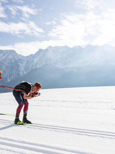 Two cross-country skiers are on the trail, one using classical technique, the other skating. Both are focused on the race, while in the background the impressive, wintry Grimming shapes the snowy landscape. | © Steiralauf/Martin Huber