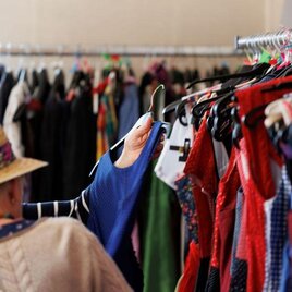 Eine Person schaut sich Kleidung in einem Modegeschäft an. Der Hintergrund zeigt eine Vielzahl von bunten Kleidungsstücken auf Kleiderständern. | © AndersOrt Haus der Frauen