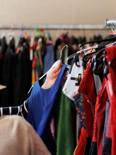 Eine Person schaut sich Kleidung in einem Modegeschäft an. Der Hintergrund zeigt eine Vielzahl von bunten Kleidungsstücken auf Kleiderständern. | © AndersOrt Haus der Frauen