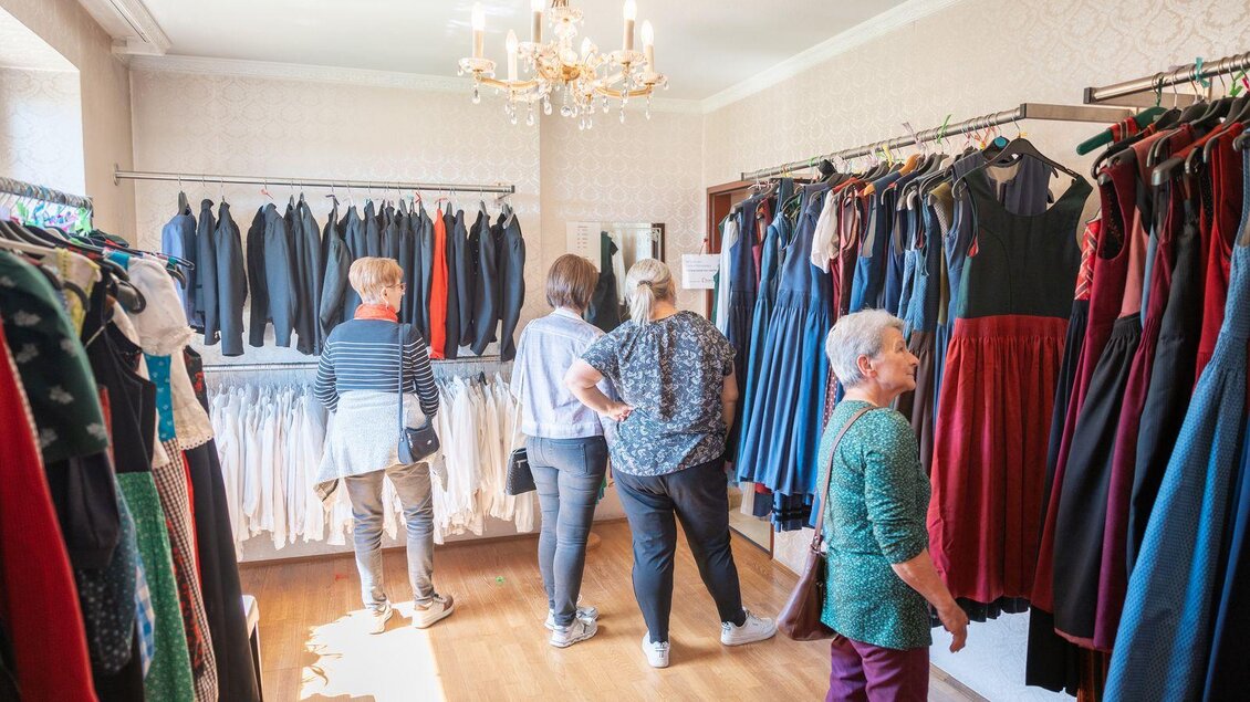 Eine Frau schaut sich Kleidungsstücke an einem Kleiderständer an. Der Hintergrund zeigt eine stilvolle Wandgestaltung. | © Haus der Frauen